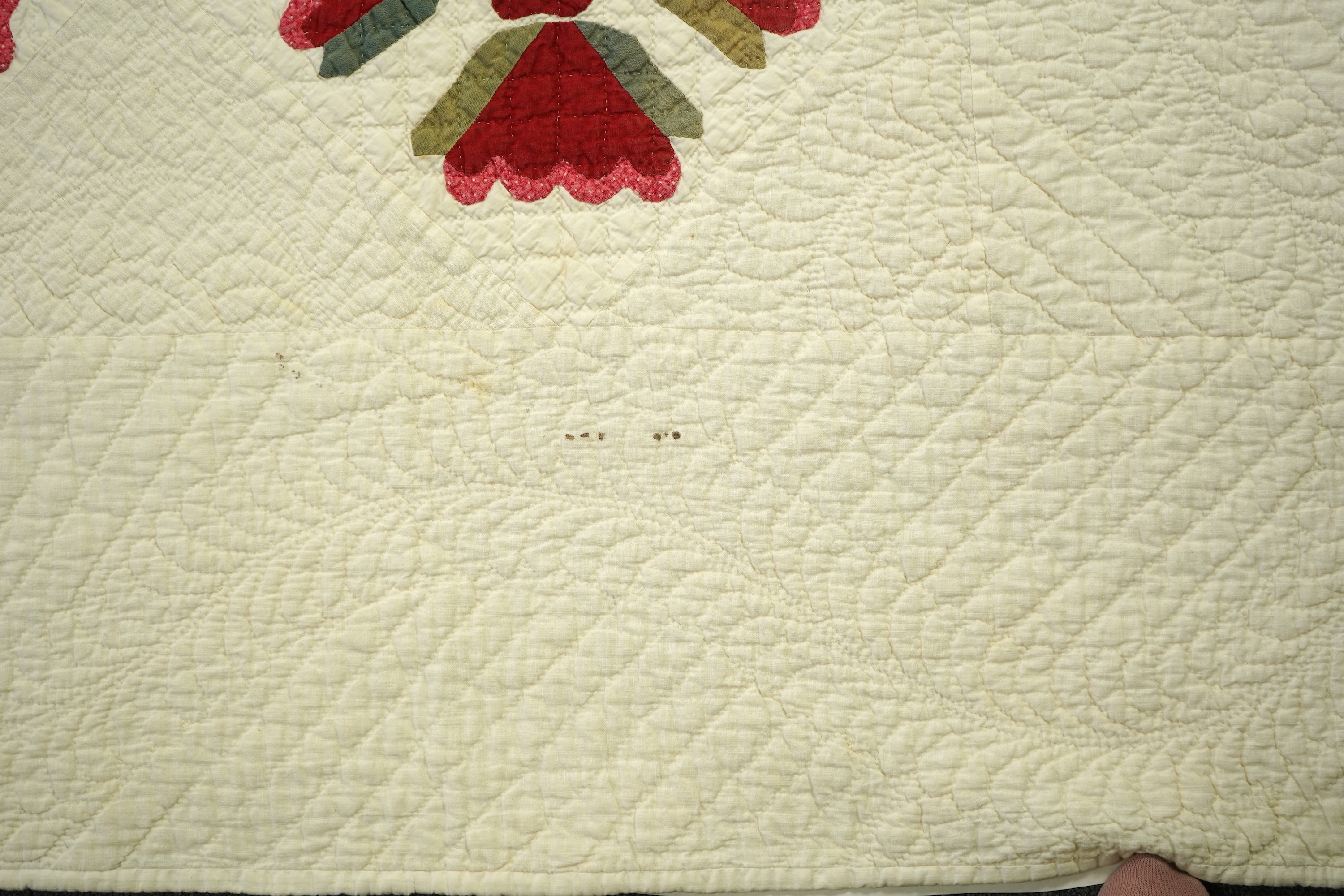 An American quilt from Kentucky, circa 1900. Intricately hand quilted on a white ground, appliquéd with stylistic repeating floral motifs in strong red and green cottons, all hand pieced. This quilt is a fine example of